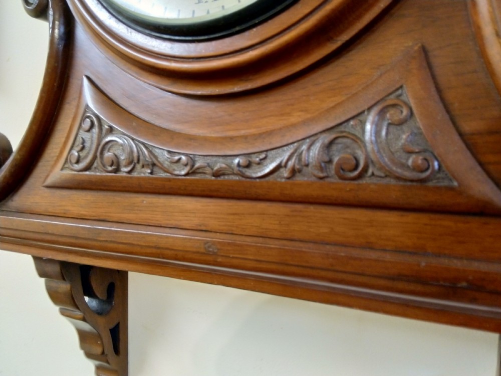 A 19th-century mahogany wall clock featuring a circular dial with Roman numerals resting on a carved wooden bracket support. View IV