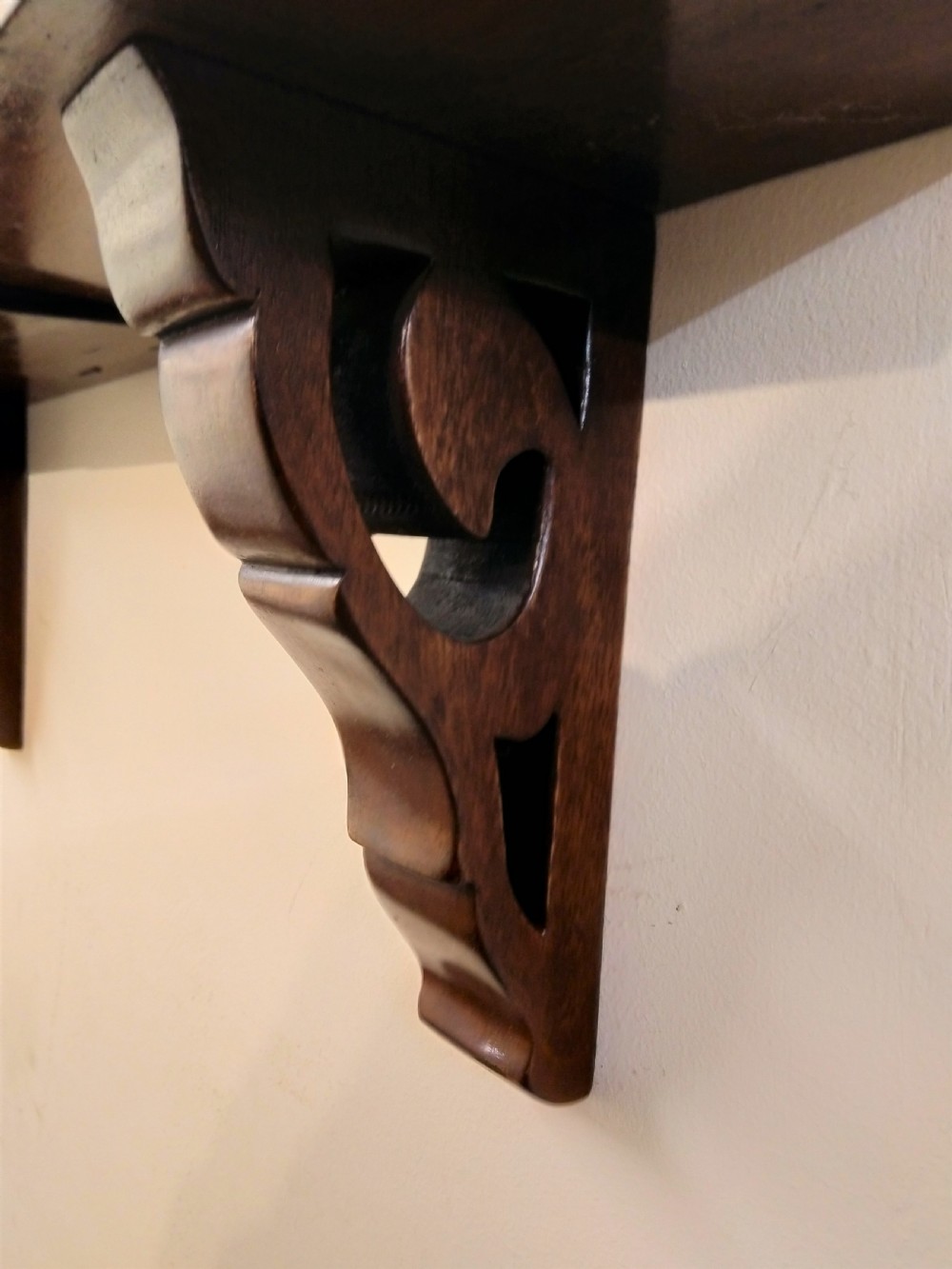 A 19th-century mahogany wall clock featuring a circular dial with Roman numerals resting on a carved wooden bracket support. View V