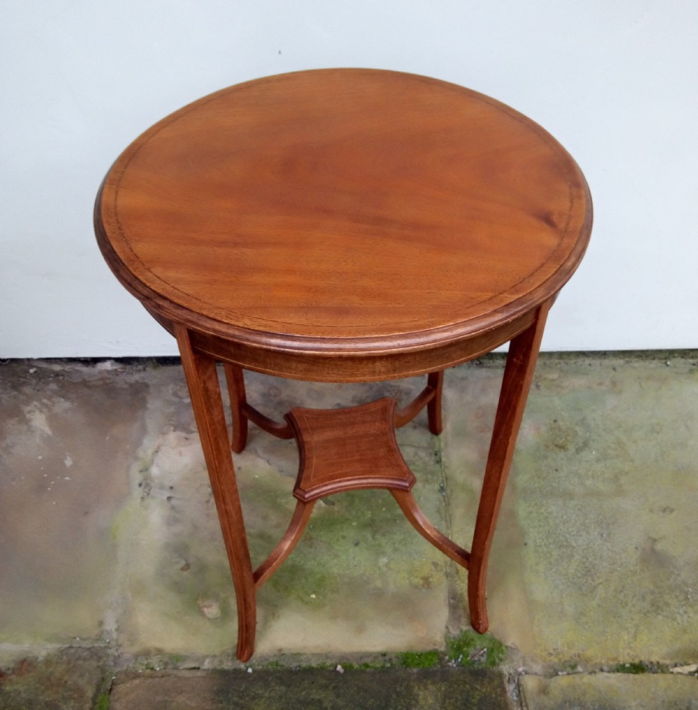 An Edwardian mahogany round occasional table featuring satinwood string inlay, slender splayed legs, and a small central undertier.