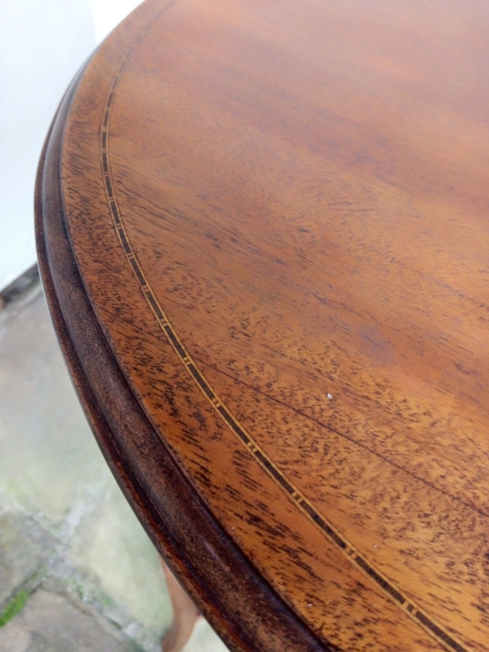 An Edwardian mahogany round occasional table featuring satinwood string inlay, slender splayed legs, and a small central undertier. View IV