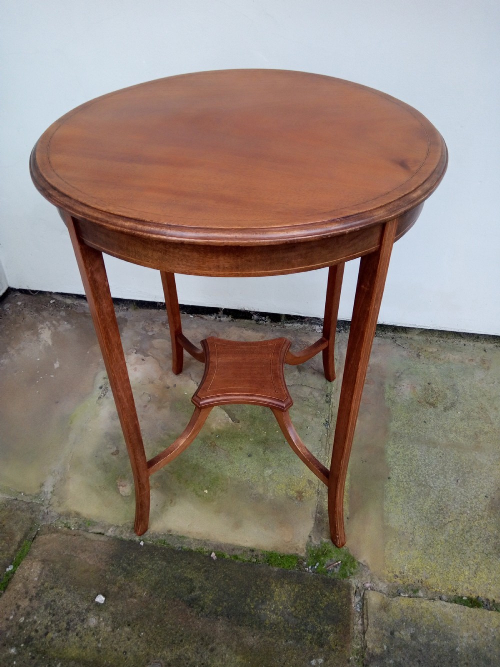 An Edwardian mahogany round occasional table featuring satinwood string inlay, slender splayed legs, and a small central undertier. View VI