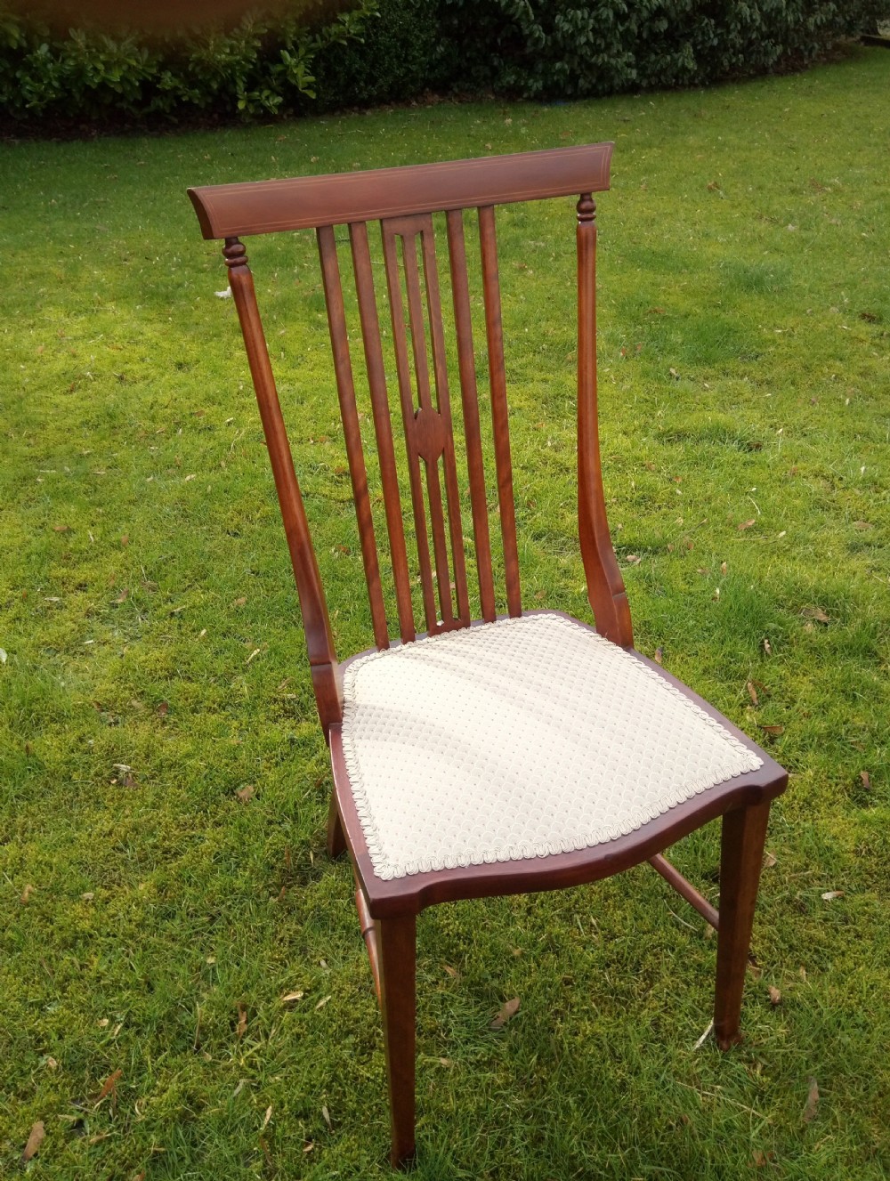 An Edwardian mahogany side chair featuring vertical back splats with fine string inlay and a cream upholstered drop-in seat.