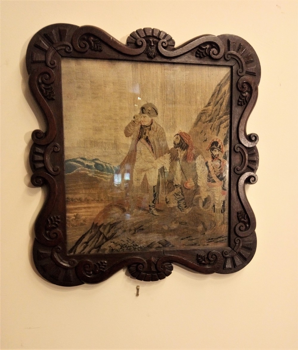 A nineteenth-century wool needlework tapestry depicting historical figures in a landscape, set within a heavily carved dark oak frame with scrollwork.
