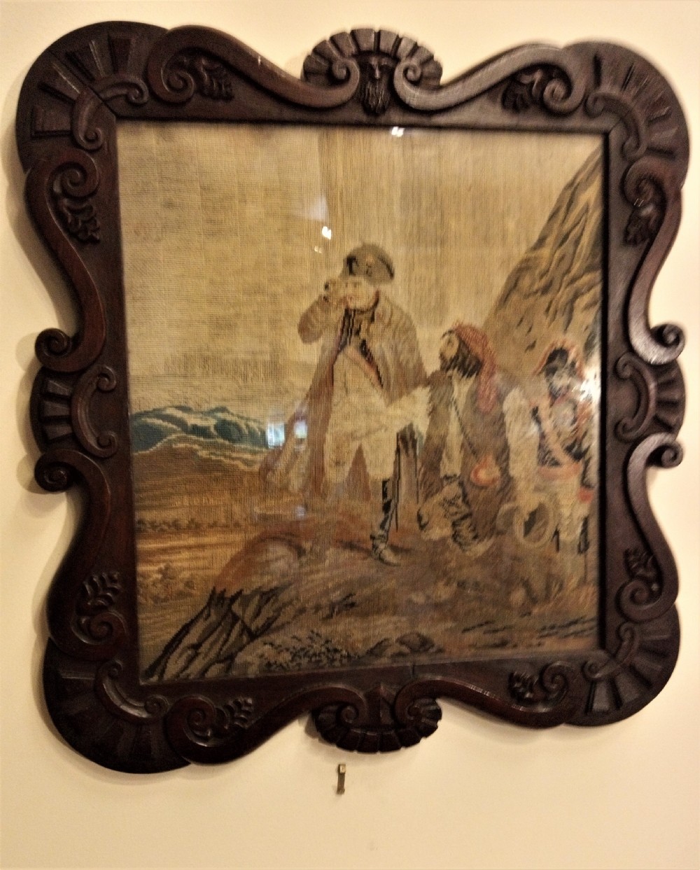 A nineteenth-century wool needlework tapestry depicting historical figures in a landscape, set within a heavily carved dark oak frame with scrollwork. View II