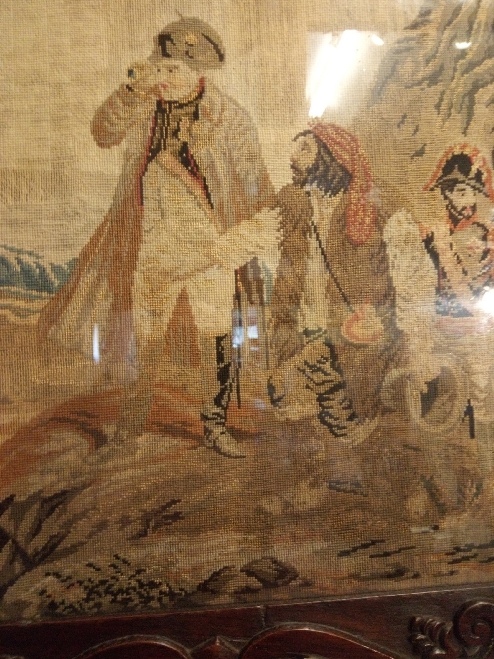 A nineteenth-century wool needlework tapestry depicting historical figures in a landscape, set within a heavily carved dark oak frame with scrollwork. View IV