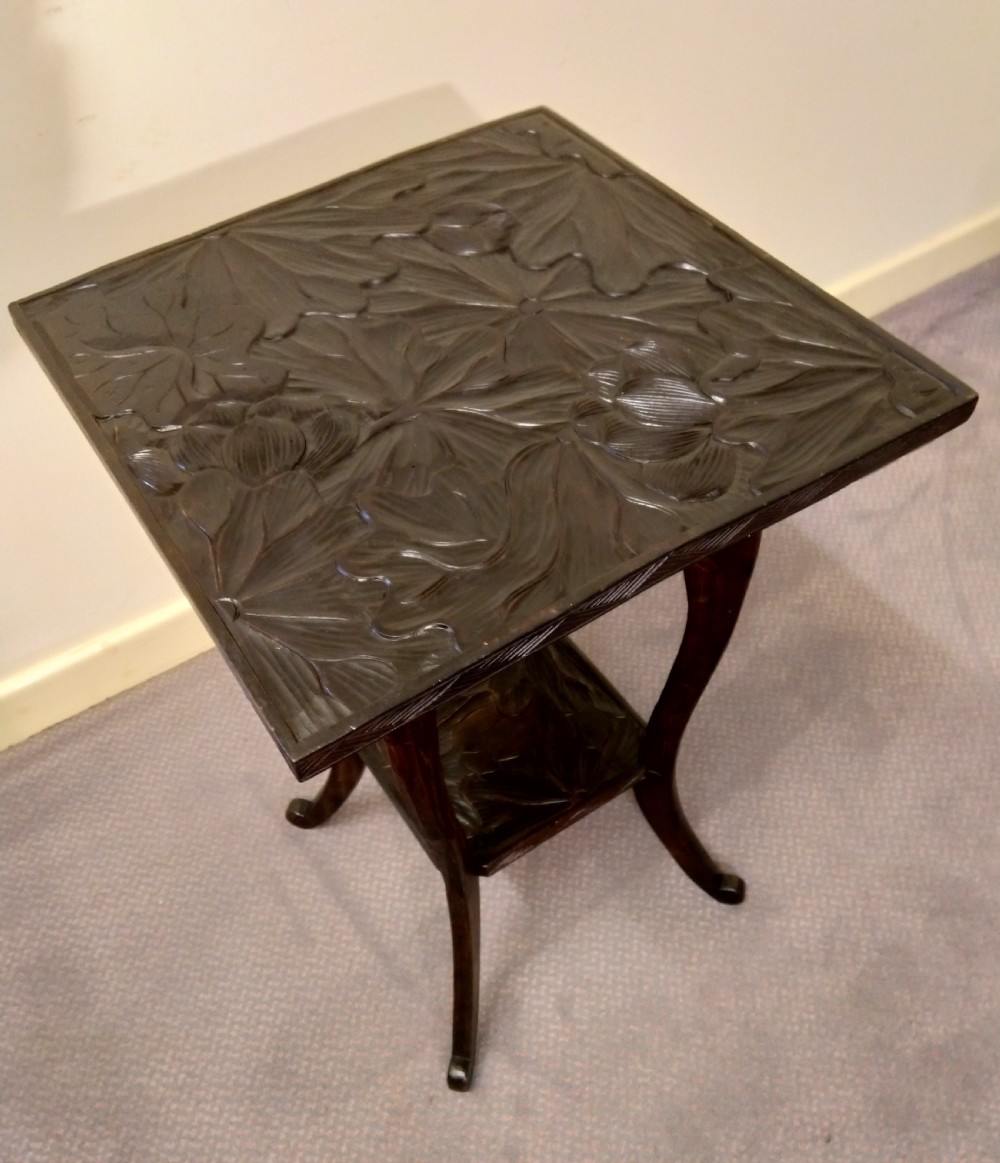 A dark brown carved wooden occasional table featuring relief botanical patterns on its square top surface and lower tier, supported by four curving legs. View II