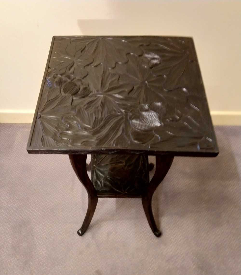 A dark brown carved wooden occasional table featuring relief botanical patterns on its square top surface and lower tier, supported by four curving legs. View III