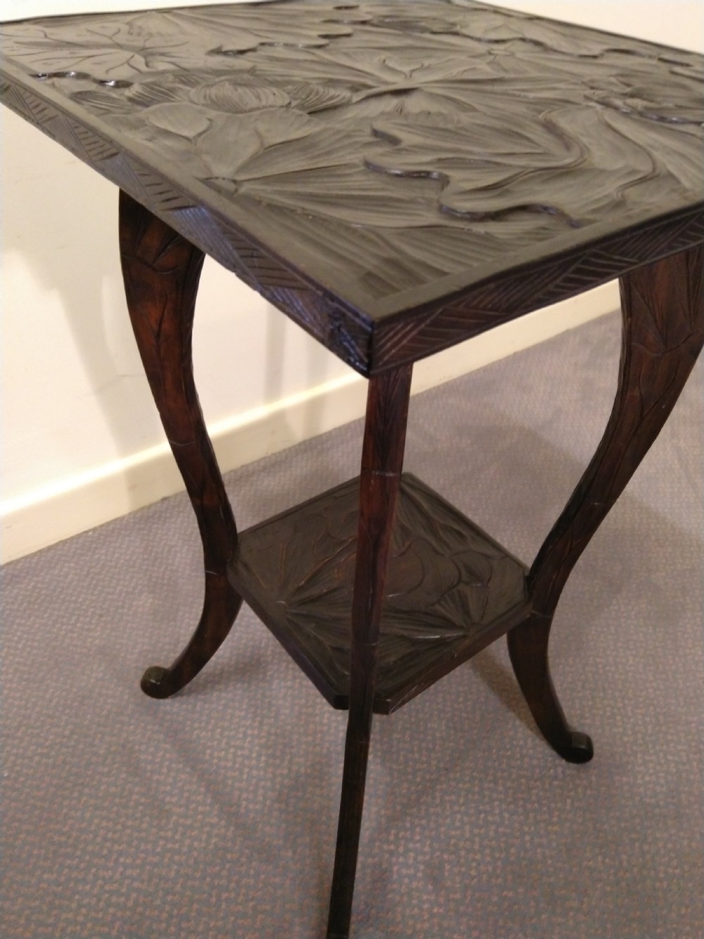 A dark brown carved wooden occasional table featuring relief botanical patterns on its square top surface and lower tier, supported by four curving legs. View V