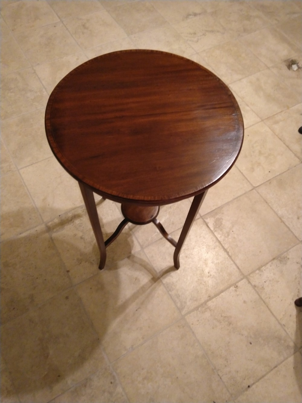A circular early 20th-century mahogany occasional table featuring a decorative inlaid top border, slender curved legs, and a circular central undertier.