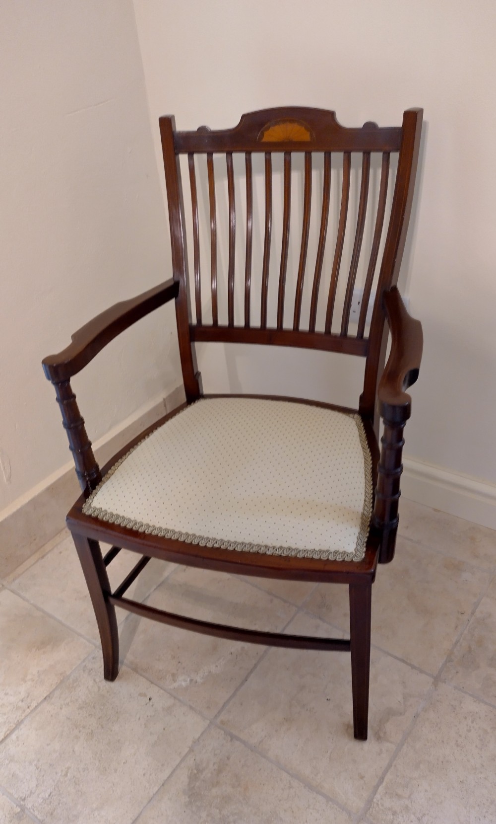 An Edwardian mahogany elbow chair featuring a vertical slat back with shell marquetry inlay, shaped arms, and a cream upholstered seat. View II
