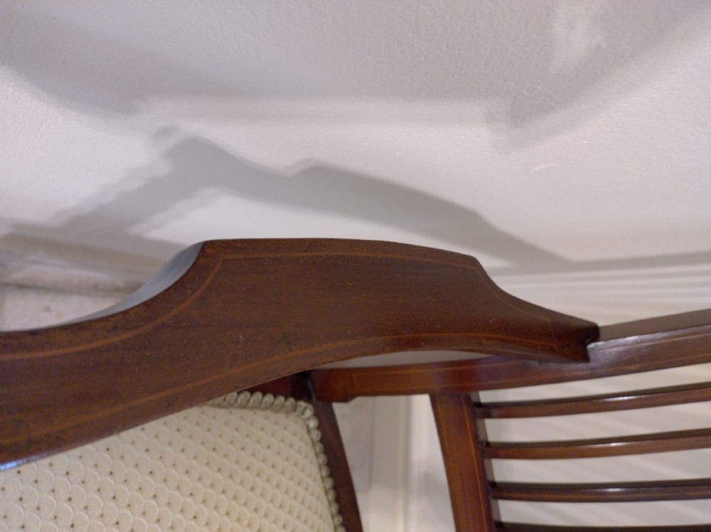 An Edwardian mahogany elbow chair featuring a vertical slat back with shell marquetry inlay, shaped arms, and a cream upholstered seat. View IV