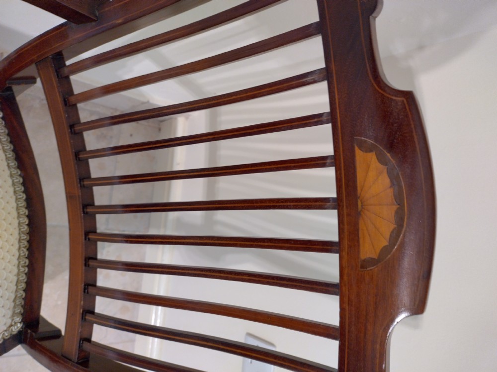 An Edwardian mahogany elbow chair featuring a vertical slat back with shell marquetry inlay, shaped arms, and a cream upholstered seat. View V