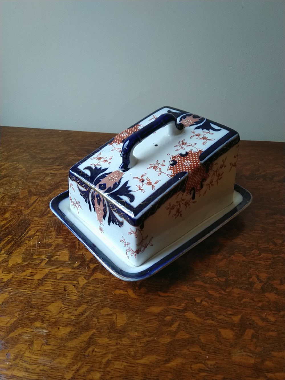 A rectangular Victorian earthenware covered cheese dish decorated with cobalt blue and terracotta Imari floral patterns on a matching tray base.