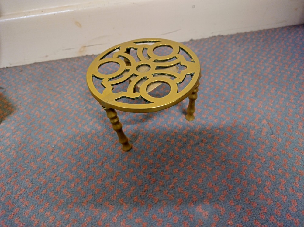 A circular cast brass trivet with a pierced geometric pattern top supported by four turned legs.