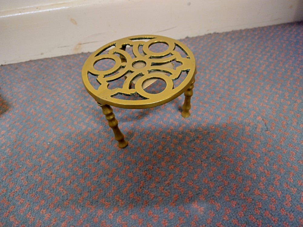 A circular cast brass trivet with a pierced geometric pattern top supported by four turned legs. View II