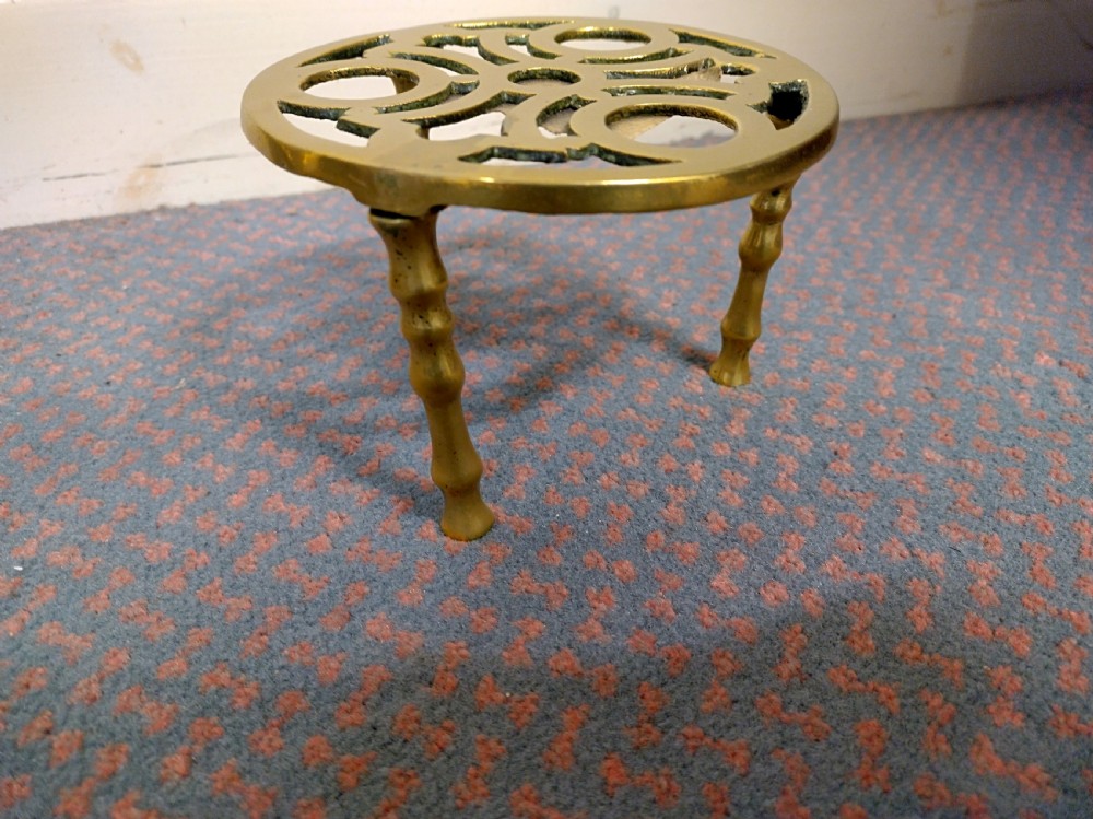 A circular cast brass trivet with a pierced geometric pattern top supported by four turned legs. View III