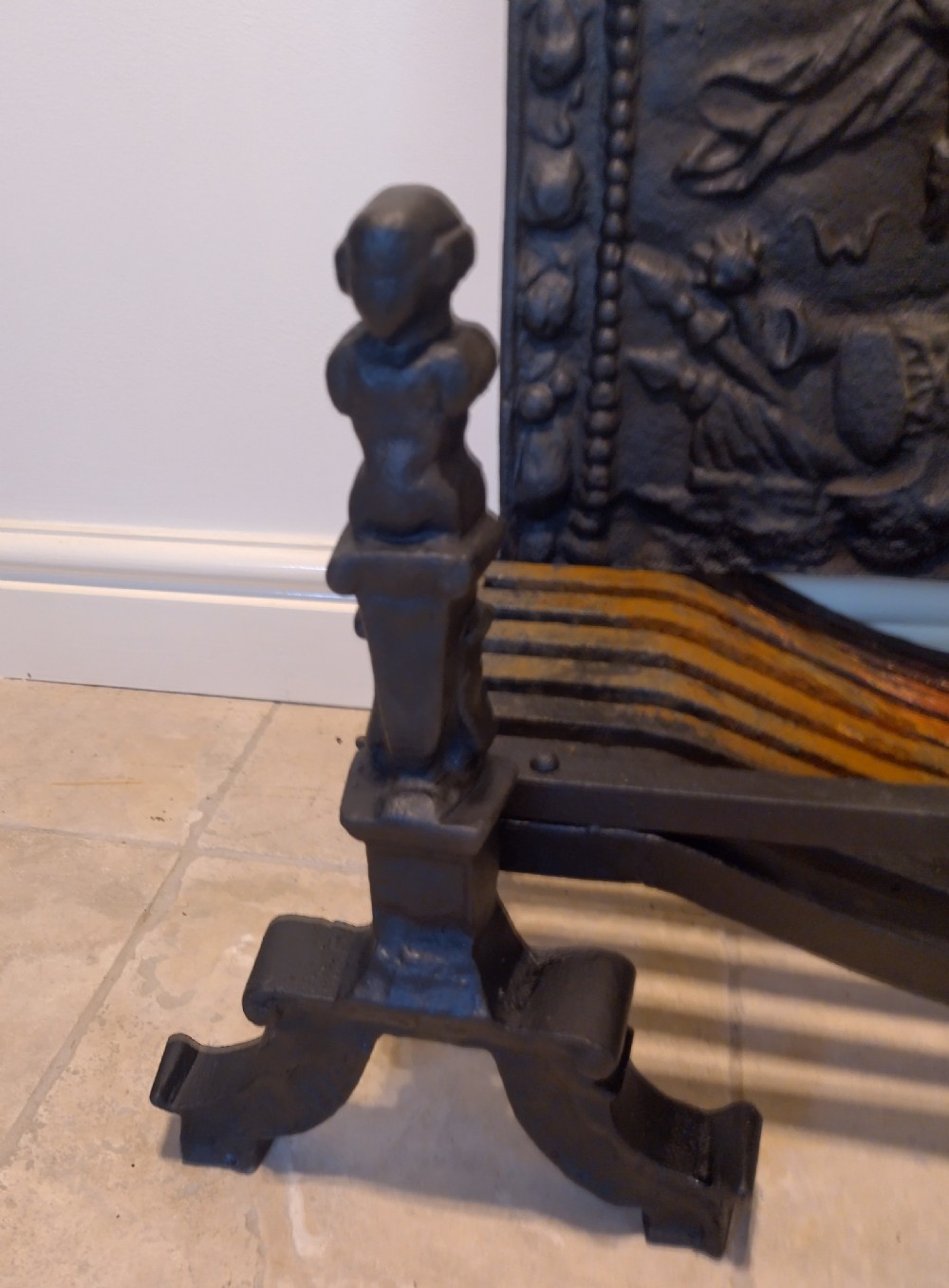 A heavy black cast iron fireback featuring pictorial relief carving, mounted above a matching fire grate with an accompanying low pierced iron fender curb. View III