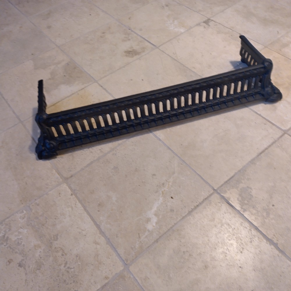 A heavy black cast iron fireback featuring pictorial relief carving, mounted above a matching fire grate with an accompanying low pierced iron fender curb. View VI