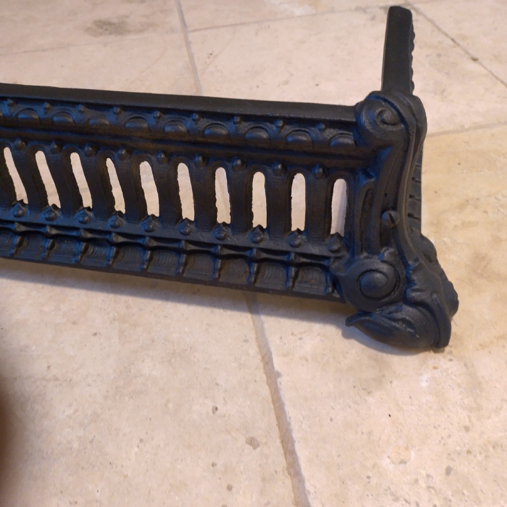 A heavy black cast iron fireback featuring pictorial relief carving, mounted above a matching fire grate with an accompanying low pierced iron fender curb. View VII