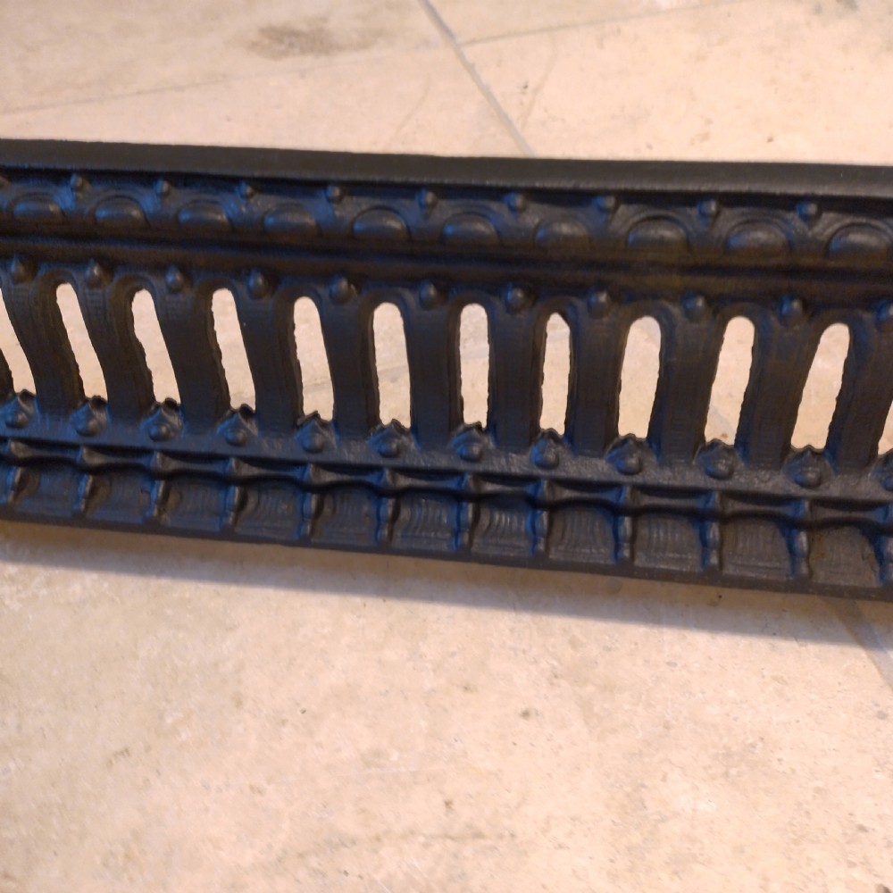 A heavy black cast iron fireback featuring pictorial relief carving, mounted above a matching fire grate with an accompanying low pierced iron fender curb. View VIII