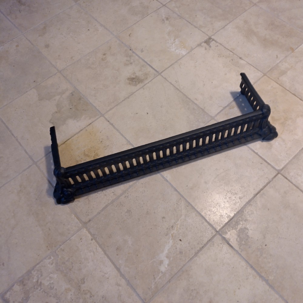 A heavy black cast iron fireback featuring pictorial relief carving, mounted above a matching fire grate with an accompanying low pierced iron fender curb. View IX