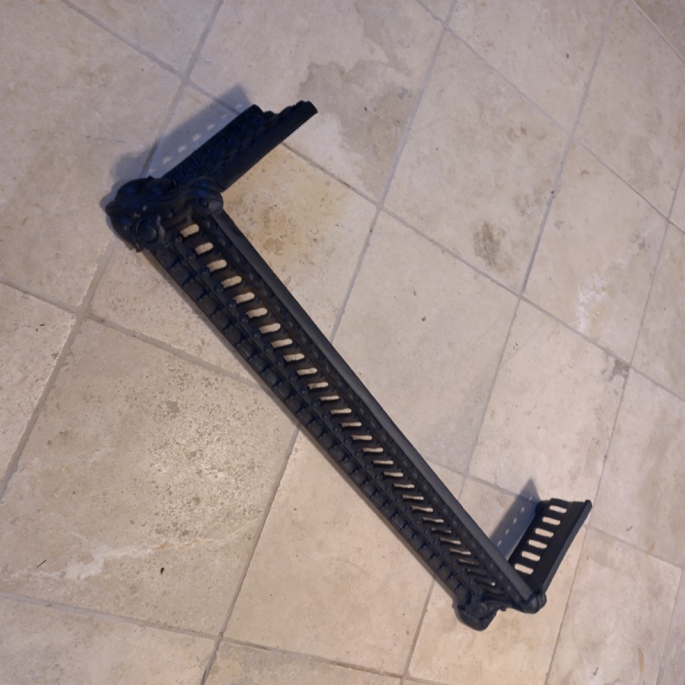 A heavy black cast iron fireback featuring pictorial relief carving, mounted above a matching fire grate with an accompanying low pierced iron fender curb. View X