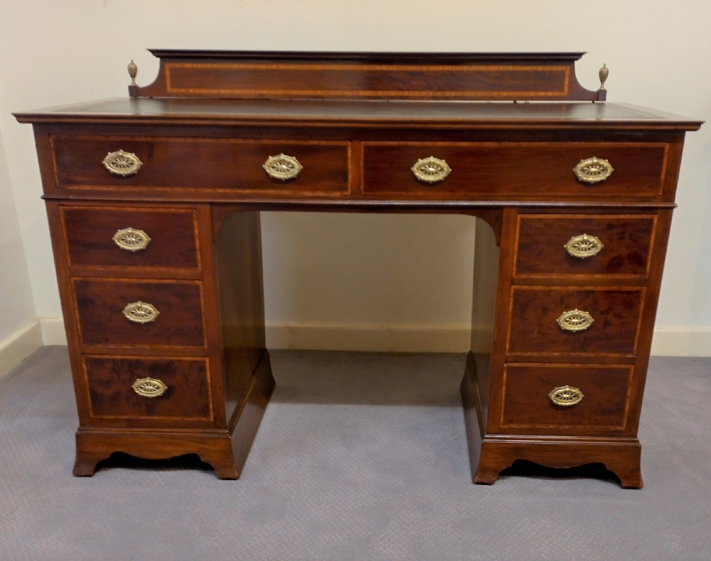 An Edwardian inlaid mahogany pedestal desk featuring twin pedestals with multiple drawers, brass oval drop handles, a dark leather writing insert, and a low gallery back with urn finials.
