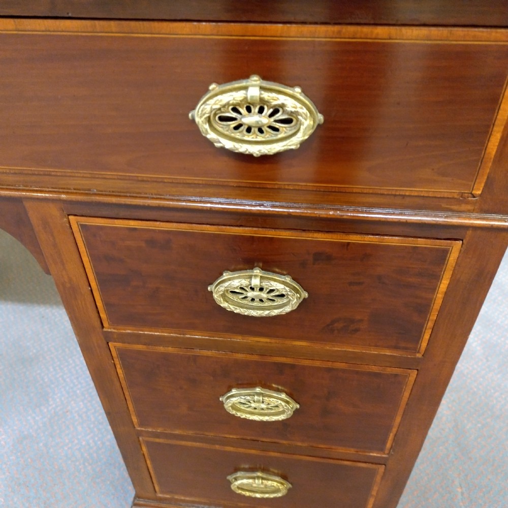 An Edwardian inlaid mahogany pedestal desk featuring twin pedestals with multiple drawers, brass oval drop handles, a dark leather writing insert, and a low gallery back with urn finials. View II