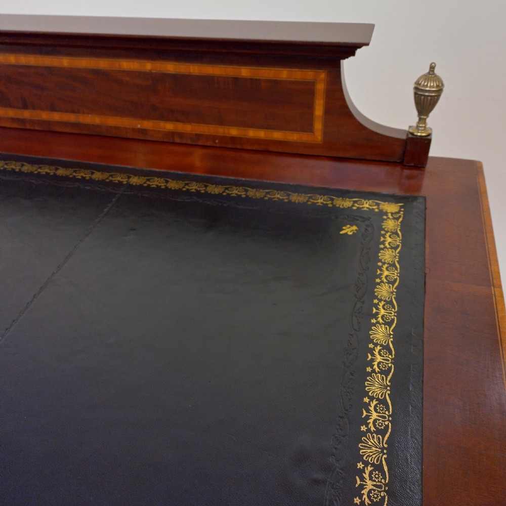 An Edwardian inlaid mahogany pedestal desk featuring twin pedestals with multiple drawers, brass oval drop handles, a dark leather writing insert, and a low gallery back with urn finials. View III