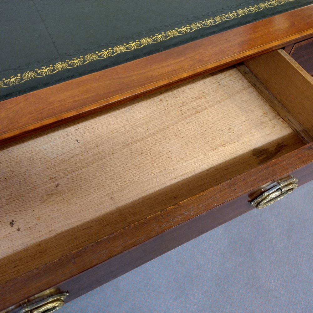 An Edwardian inlaid mahogany pedestal desk featuring twin pedestals with multiple drawers, brass oval drop handles, a dark leather writing insert, and a low gallery back with urn finials. View VI