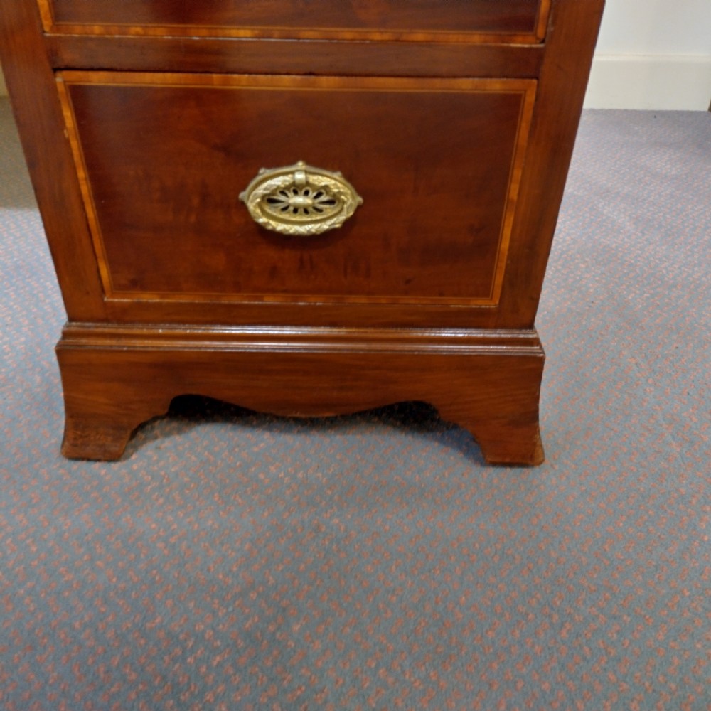 An Edwardian inlaid mahogany pedestal desk featuring twin pedestals with multiple drawers, brass oval drop handles, a dark leather writing insert, and a low gallery back with urn finials. View VIII