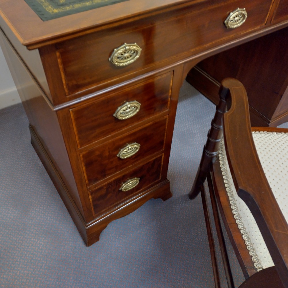 An Edwardian inlaid mahogany pedestal desk featuring twin pedestals with multiple drawers, brass oval drop handles, a dark leather writing insert, and a low gallery back with urn finials. View IX