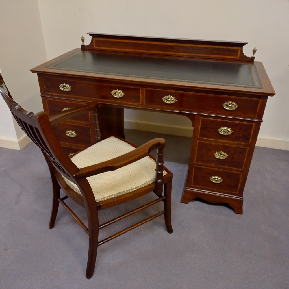 An Edwardian inlaid mahogany pedestal desk featuring twin pedestals with multiple drawers, brass oval drop handles, a dark leather writing insert, and a low gallery back with urn finials. View X