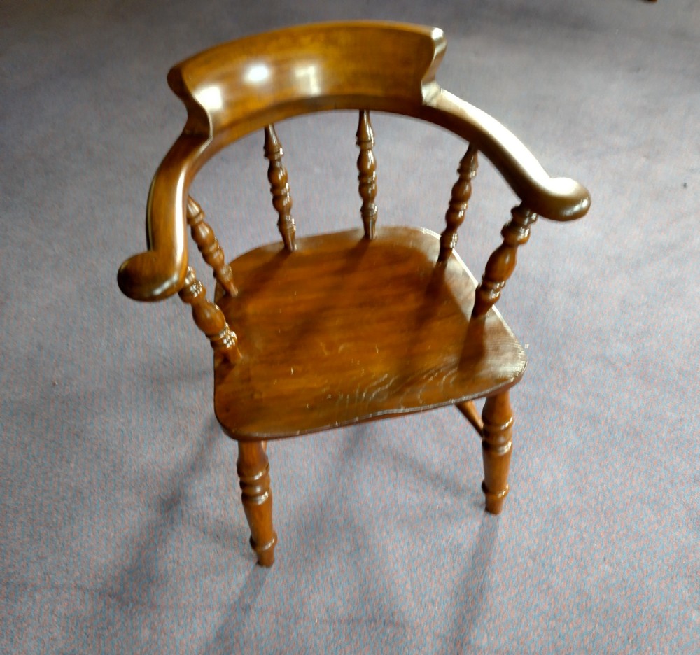 A 19th-century wooden captains chair featuring turned spindles, a curved horseshoe armrest with scrolled terminals, and a solid saddle seat.