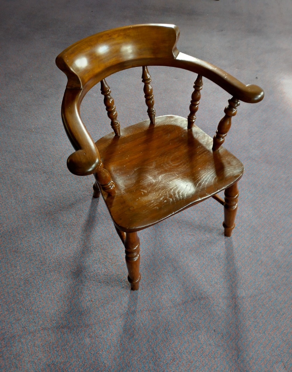 A 19th-century wooden captains chair featuring turned spindles, a curved horseshoe armrest with scrolled terminals, and a solid saddle seat. View II