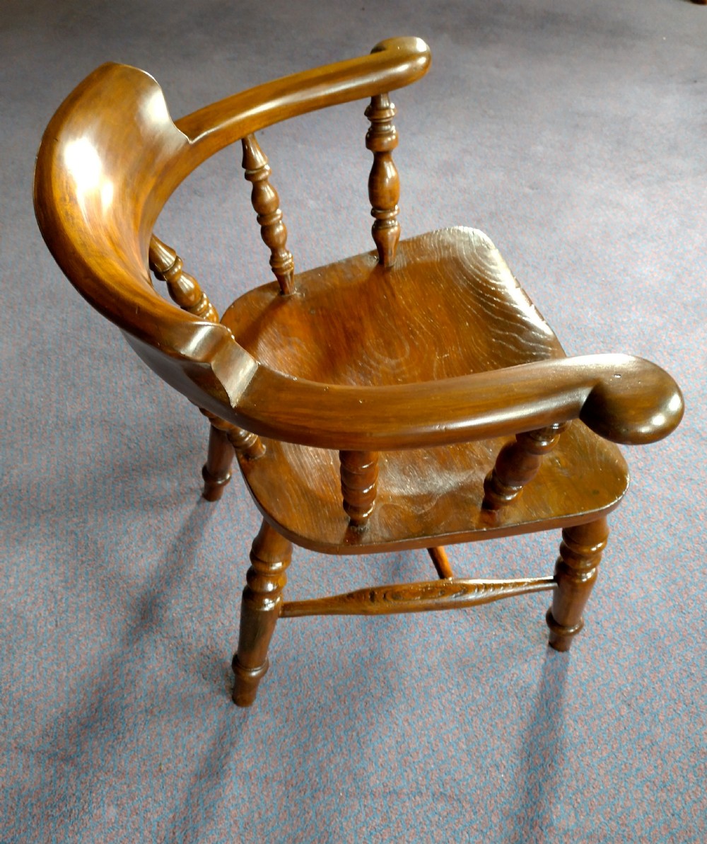 A 19th-century wooden captains chair featuring turned spindles, a curved horseshoe armrest with scrolled terminals, and a solid saddle seat. View V