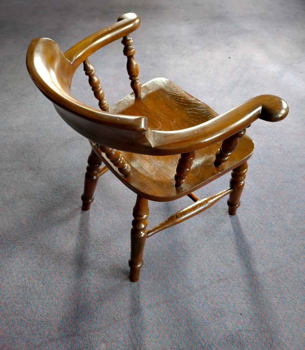 A 19th-century wooden captains chair featuring turned spindles, a curved horseshoe armrest with scrolled terminals, and a solid saddle seat. View VI
