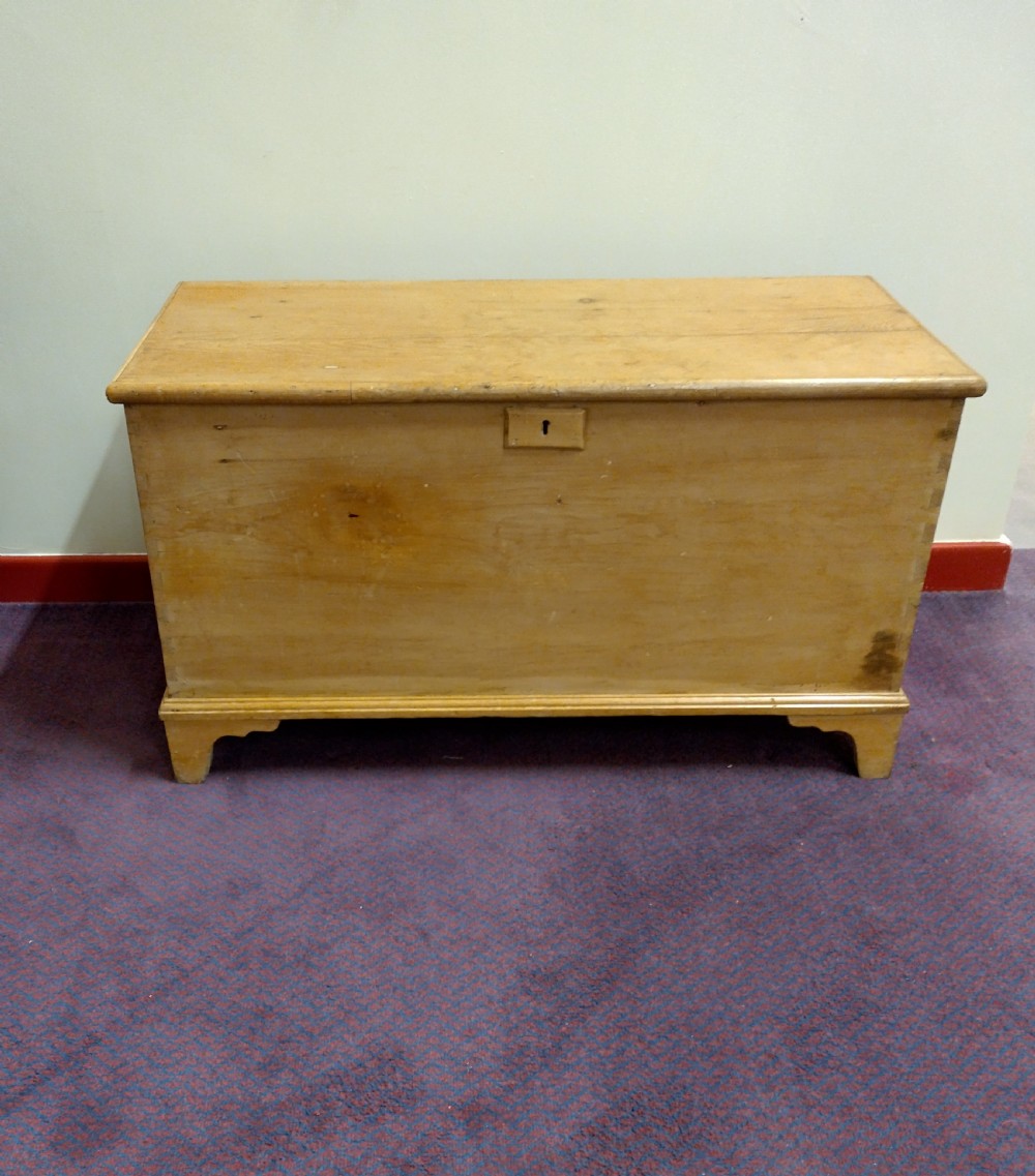 A nineteenth-century rectangular pine bedding chest with a hinged lid, brass keyhole escutcheon, and shaped bracket feet.