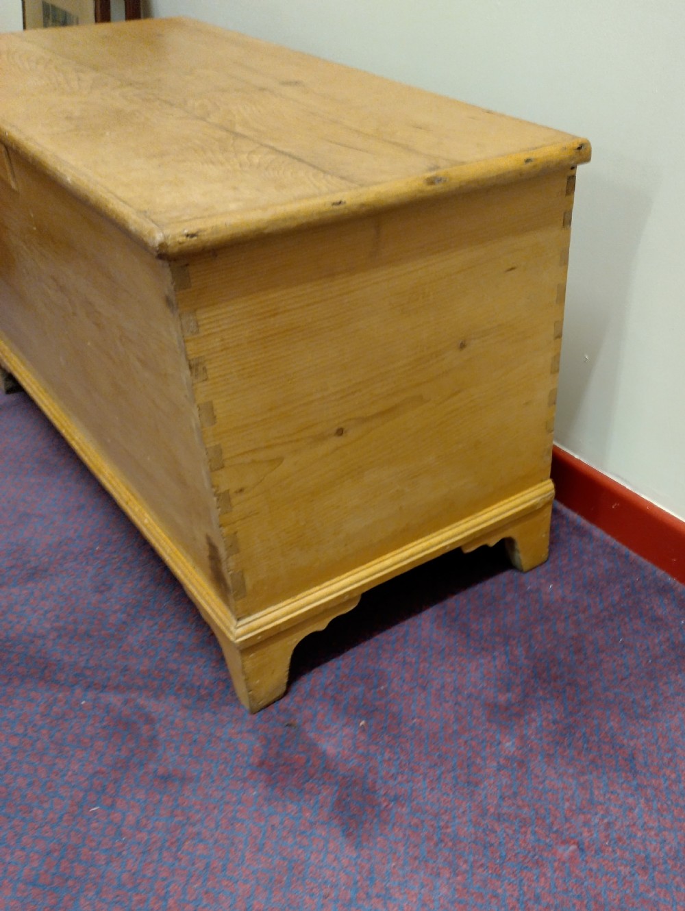 A nineteenth-century rectangular pine bedding chest with a hinged lid, brass keyhole escutcheon, and shaped bracket feet. View VI