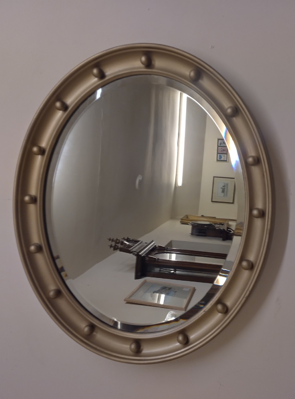 An oval wall mirror featuring a gilt metal frame decorated with raised spherical studs around its border and a bevelled glass mirror plate. View II