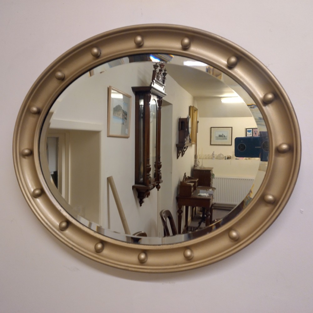 An oval wall mirror featuring a gilt metal frame decorated with raised spherical studs around its border and a bevelled glass mirror plate.