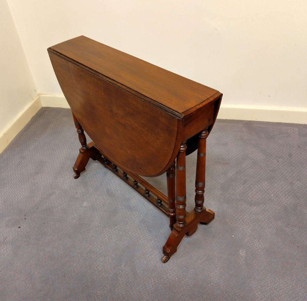 A late Victorian mahogany Sutherland table with an oval drop-leaf top, turned leg supports, lower spindle stretcher, and brass castors. View IV