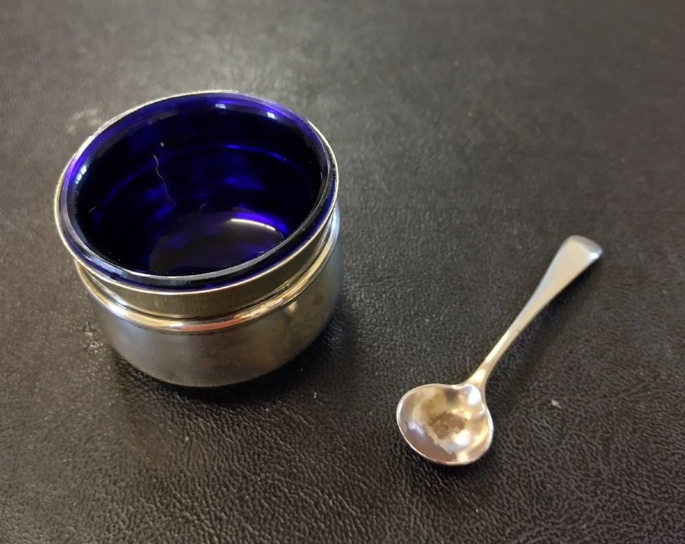 A circular sterling silver salt cellar with a cobalt blue glass liner insert and a silver salt spoon. View II