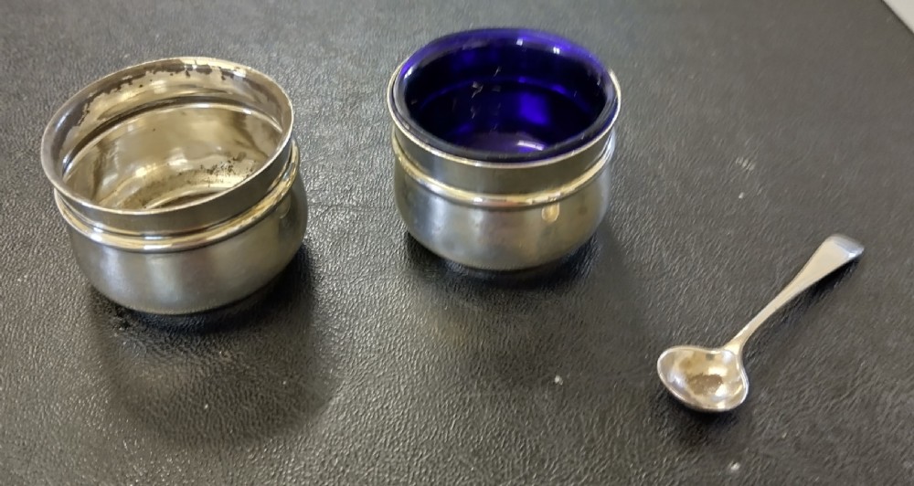 A circular sterling silver salt cellar with a cobalt blue glass liner insert and a silver salt spoon. View III