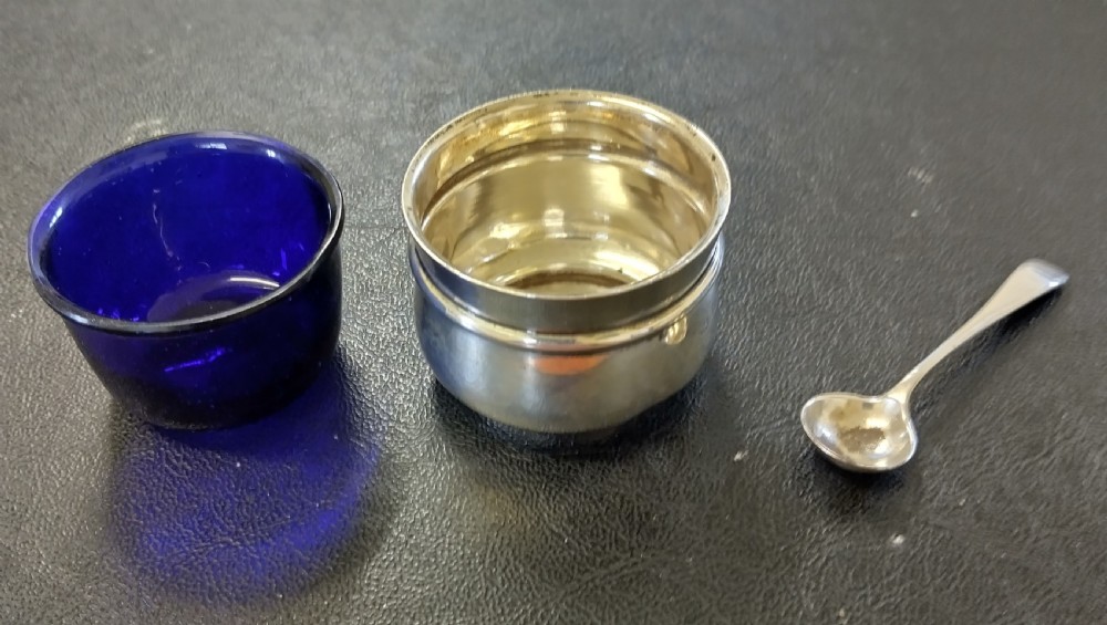 A circular sterling silver salt cellar with a cobalt blue glass liner insert and a silver salt spoon. View V