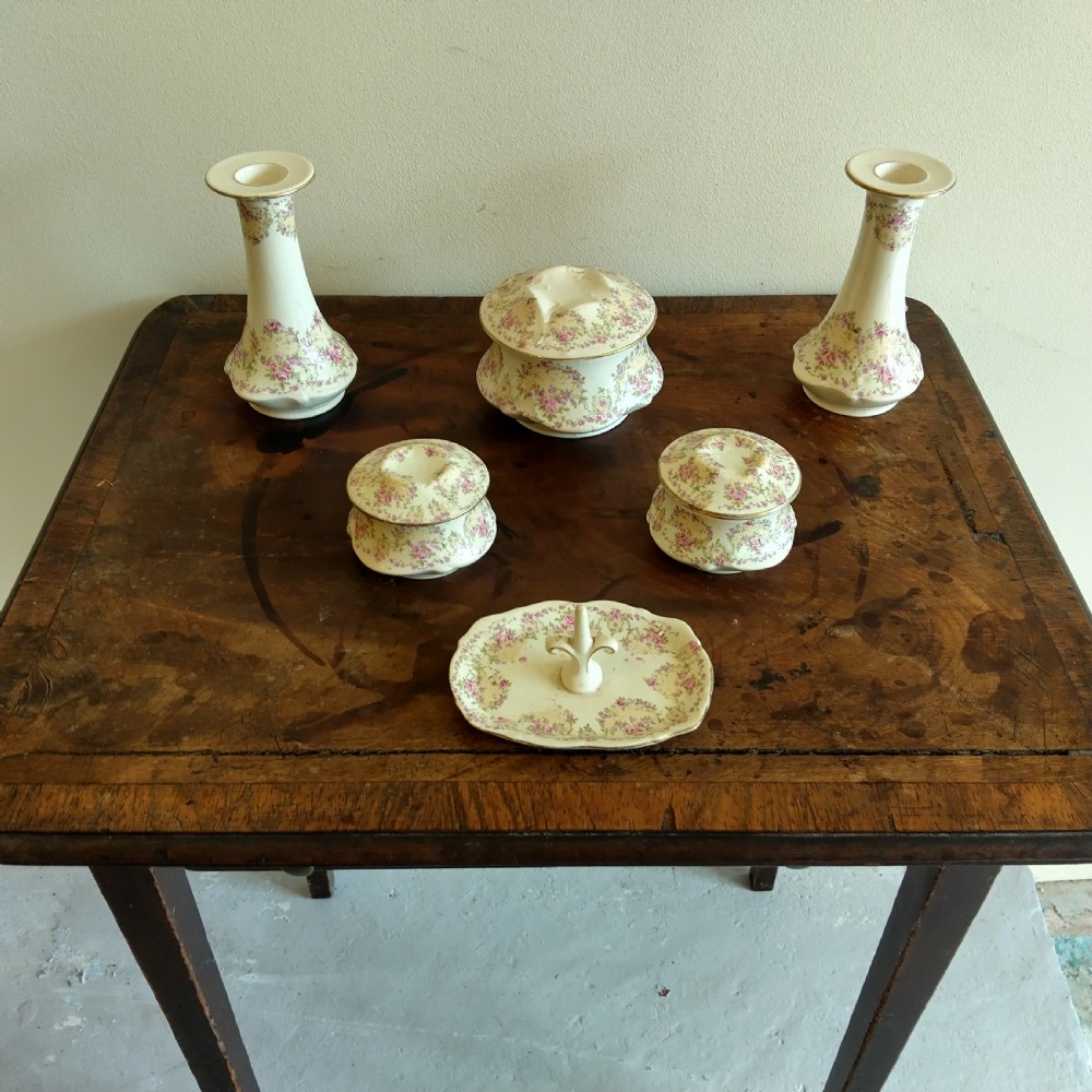 A six-piece cream porcelain dressing table set decorated with pink floral transfer patterns, gilt rims, two candlesticks, three lidded pots, and a ring tray.