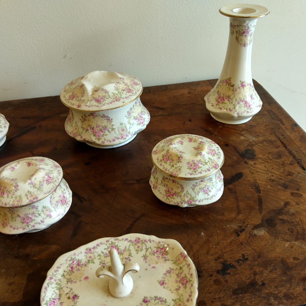 A six-piece cream porcelain dressing table set decorated with pink floral transfer patterns, gilt rims, two candlesticks, three lidded pots, and a ring tray. View III
