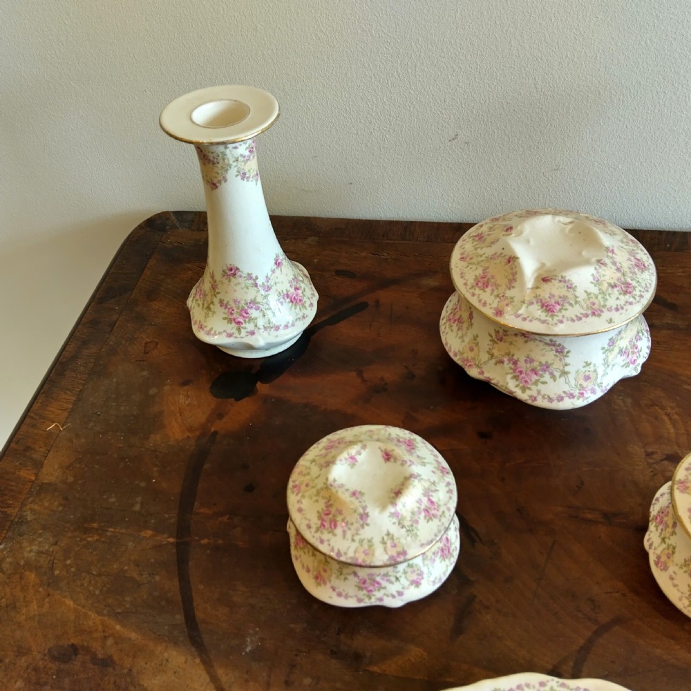 A six-piece cream porcelain dressing table set decorated with pink floral transfer patterns, gilt rims, two candlesticks, three lidded pots, and a ring tray. View IV