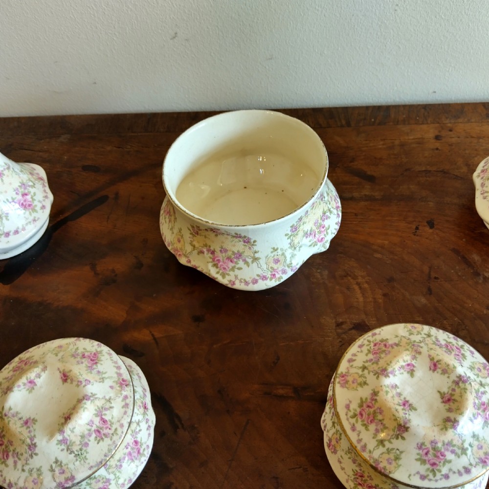 A six-piece cream porcelain dressing table set decorated with pink floral transfer patterns, gilt rims, two candlesticks, three lidded pots, and a ring tray. View V