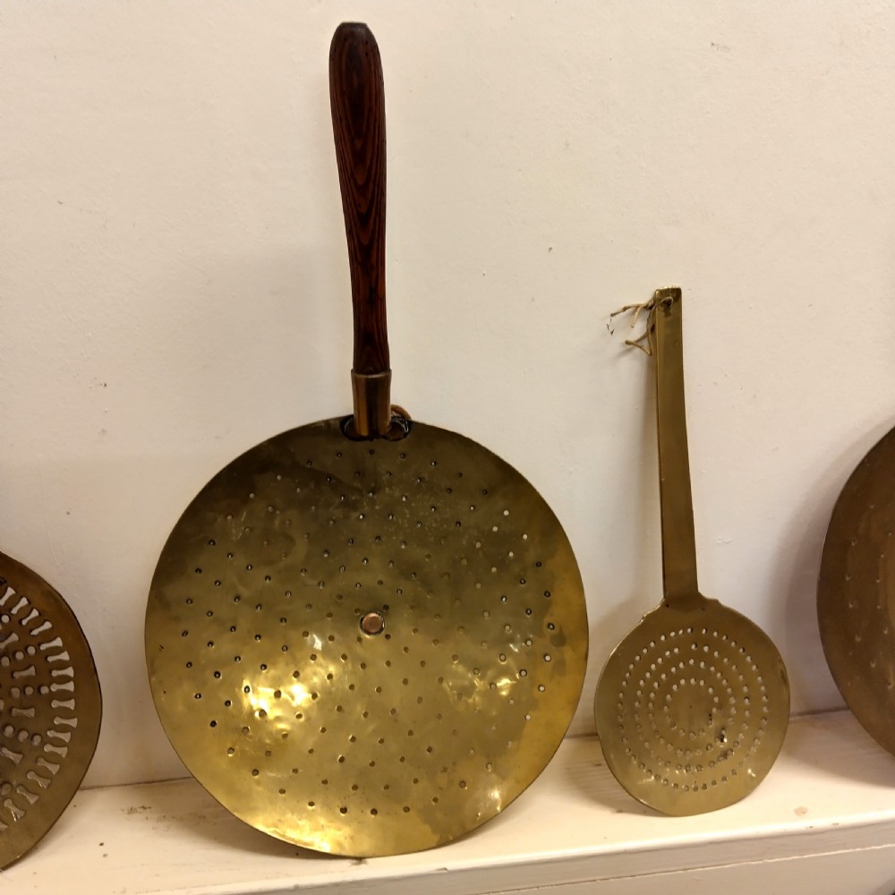 A collection of four antique brass cream skimmers with pierced round bowls, featuring turned wooden handles and decorative flat brass handles. View III